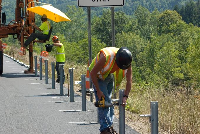 Workers installing W Beam Guardrail posts along a roadside